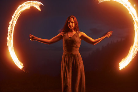 Photo with a long exposure. Fire show by woman in dress in night Carphatian mountains. Beautiful landscapeの写真素材