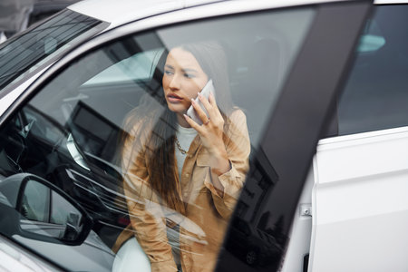 Talks by phone with door opened. Fashionable beautiful young woman and her modern automobileの写真素材