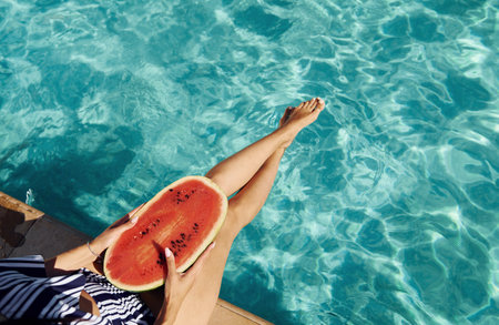 Young woman sits near swimming pool at daytime with watermelonの写真素材