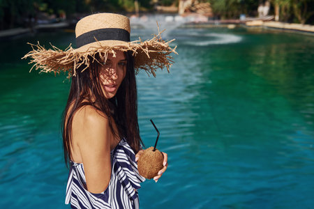 In straw hat. Girl have fun and rest in swimming pool at daytime. Conception of vacationの写真素材