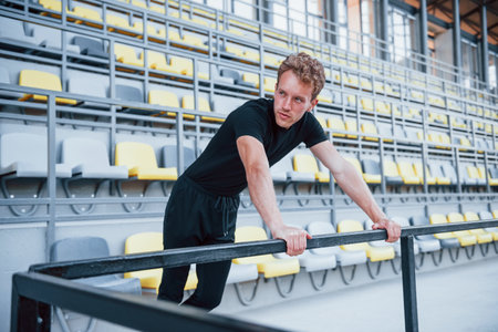 Leaning on the railings. Sportive young guy in black shirt and pants outdoors at daytimeの写真素材