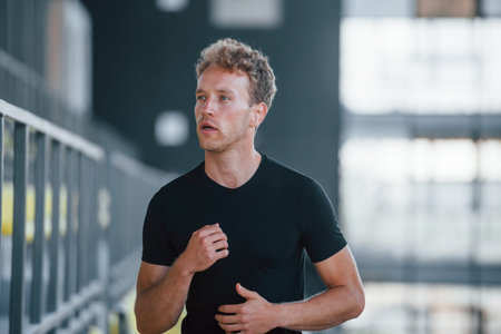 Running on the bleachers. Sportive young guy in black shirt and pants outdoors at daytime