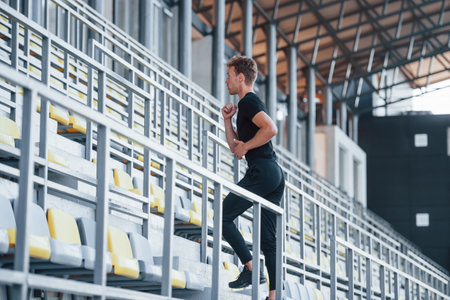 Running on stairs. Sportive young guy in black shirt and pants outdoors at daytimeの写真素材