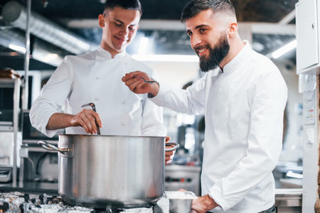 With help from other employee. Chef in white uniform cooking food at kitchen. Busy day at work