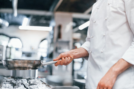Making delicious product. Chef in white uniform cooking food at kitchen. Busy day at workの写真素材