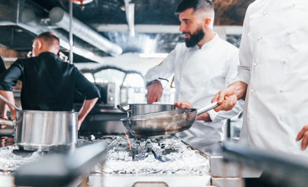 People in white uniform cooking food at kitchen together. Busy day at workの写真素材