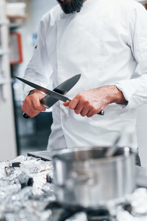 Chef in white uniform standing at kitchen. Holding knives in handsの写真素材