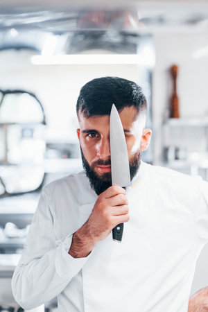 Chef in white uniform standing at kitchen. Holding knife in handsの写真素材