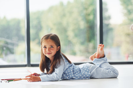 Lying on the floor and drawing. Cute little girl indoors at home aloneの写真素材