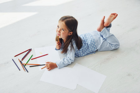 Lying on the floor and drawing. Cute little girl indoors at home aloneの写真素材