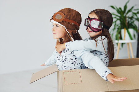 Sitting in the paper box. Two cute little girls indoors at home together. With retro pilot glasses...
