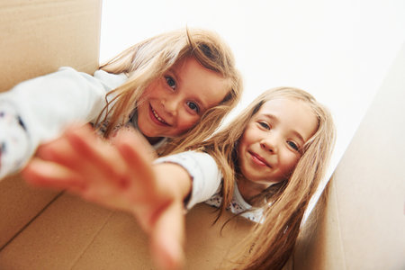 Looking inside of paper box. Two cute little girls indoors at home together. Children having funの写真素材