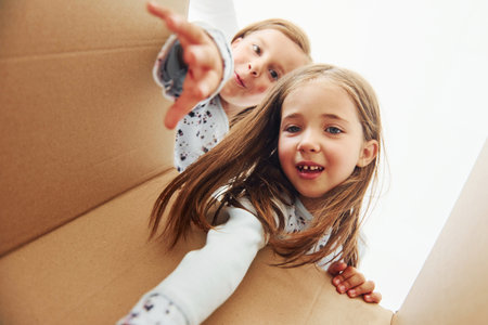 Looking inside of paper box. Two cute little girls indoors at home together. Children having funの写真素材