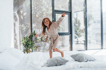 Jumping on the sofa. Cute little girl indoors at home alone. Child enjoying weekendの写真素材
