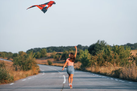 Young cheerful woman having fun with kite outdoors on the roadの写真素材