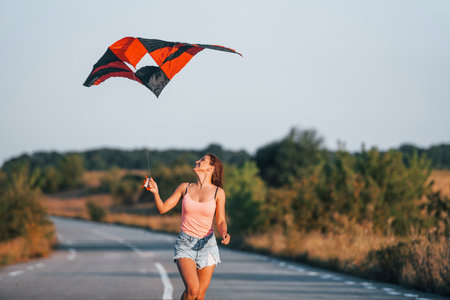 Young cheerful woman having fun with kite outdoors on the roadの写真素材