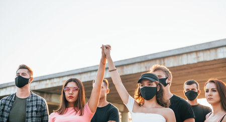 Fists rased high up. Group of protesting young people that standing together. Activist for human...