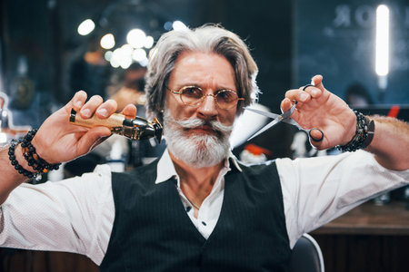 Holds barbershop equipment. Stylish modern senior man with gray hair and beard is indoorsの写真素材