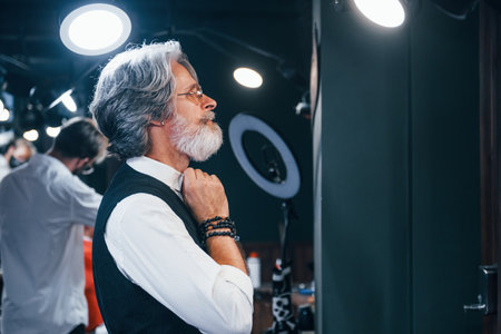 In retro clothes in barbershop. Stylish modern senior man with gray hair and beard is indoorsの写真素材