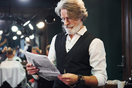 Reading newspaper. Stylish modern senior man with gray hair and beard is indoorsの写真素材