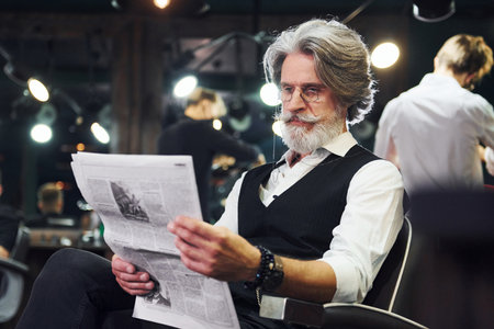 Reading newspaper. Stylish modern senior man with gray hair and beard is indoorsの写真素材