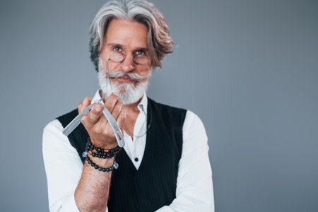 Barbershop tools. Against grey background. Stylish modern senior man with gray hair and beard is indoorsの写真素材