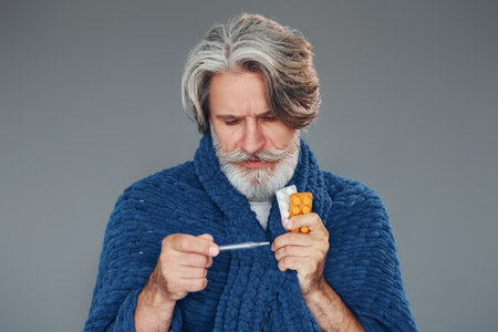 Getting sick. Against grey background. Stylish modern senior man with gray hair and beard is indoorsの写真素材