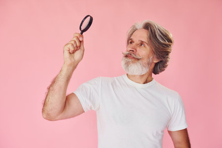 Using magnifying glass. Stylish modern senior man with gray hair and beard is indoorsの写真素材