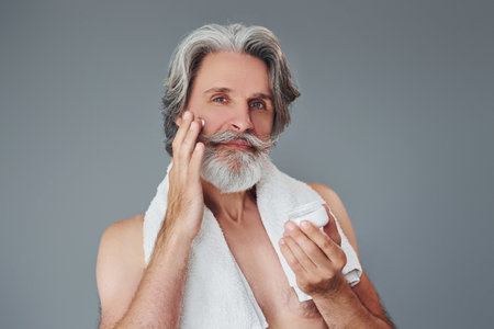 Taking care of face and skin clearness. Stylish modern senior man with gray hair and beard is indoorsの写真素材