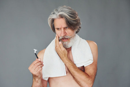 Conception of shaving. Stylish modern senior man with gray hair and beard is indoorsの写真素材