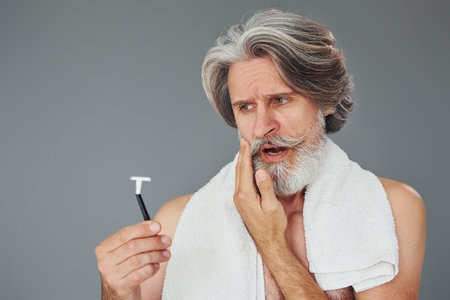 Conception of shaving. Stylish modern senior man with gray hair and beard is indoorsの写真素材