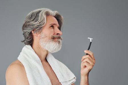 Conception of shaving. Stylish modern senior man with gray hair and beard is indoorsの写真素材