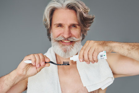 Using toothpaste. Stylish modern senior man with gray hair and beard is indoorsの写真素材