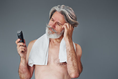 Taking care of beard. Stylish modern senior man with gray hair is indoorsの写真素材