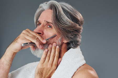 Taking care of beard. Stylish modern senior man with gray hair is indoorsの写真素材