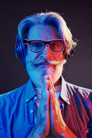 Neon lighting, conception of party. Stylish modern senior man with gray hair and beard is indoorsの写真素材