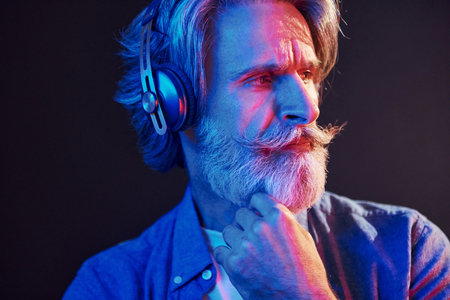 Beautiful neon lighting. Stylish modern senior man with gray hair and beard is indoorsの写真素材