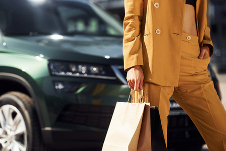 With paper bag in hand. Young fashionable woman in burgundy colored coat at daytime with her carの写真素材