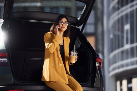 Talks by phone. Young fashionable woman in burgundy colored coat at daytime with her carの写真素材