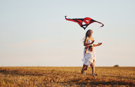 Happy mother with her little daughter have fun by playing with kite outdoors on the fieldの写真素材