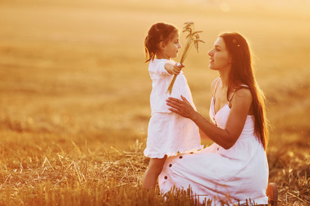 Positive little girl with her mother have weekend outdoors on the summer field togetherの写真素材