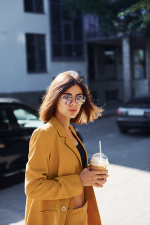 Coffee break. Young fashionable woman in burgundy colored coat at daytime with her carの写真素材