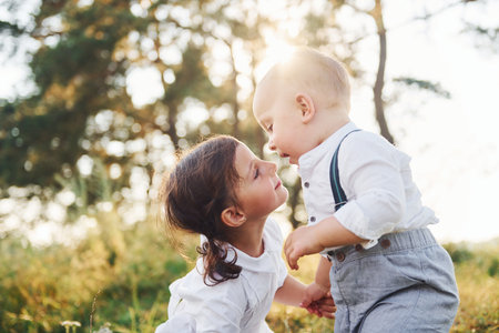 Cute brother and sister playing together outdoors with beautiful trees and sunshine at backgroundの写真素材