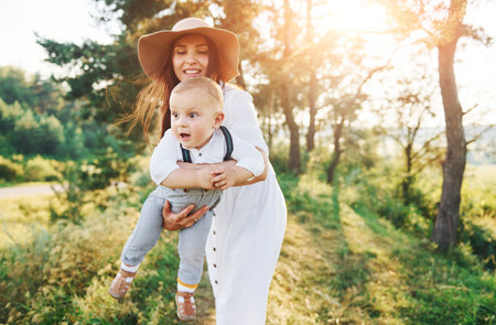 Young mother with her little son is outdoors in the forest. Beautiful sunshine