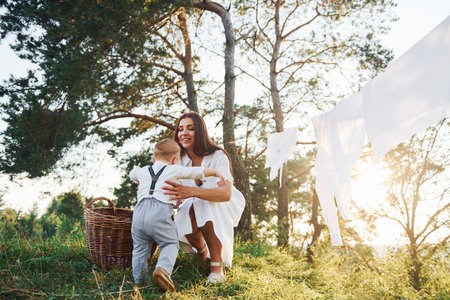 Clean clothes hanging on the rope to dry. Young mother with her little son is outdoors in the...
