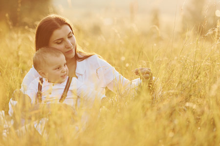 Young mother with her little son is outdoors in the agricultural field. Beautiful sunshineの写真素材