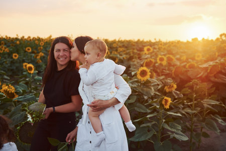Young mother with her little son, daughter and female friend is outdoors in the agricultural field. Beautiful sunshineの写真素材
