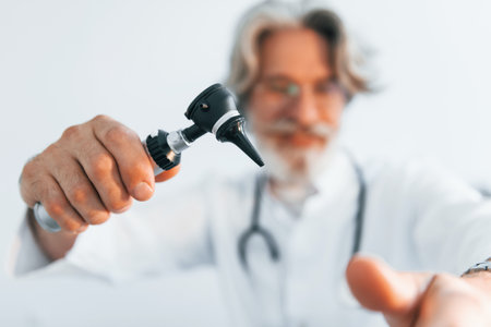 Portrait of senior male doctor with grey hair and beard in white coat is indoors in otorhinolaryngology clinicの写真素材