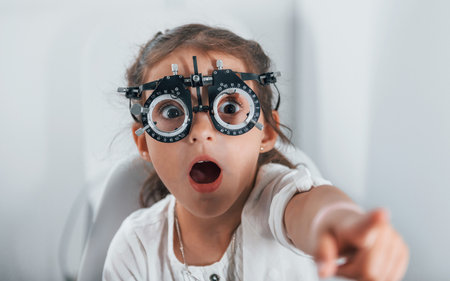 Cute little girl is in ophthalmology clinic with special tool on eyes getting testedの写真素材