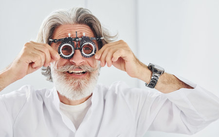 Nice facial expressions. Senior man with grey hair and beard is in ophthalmology clinic